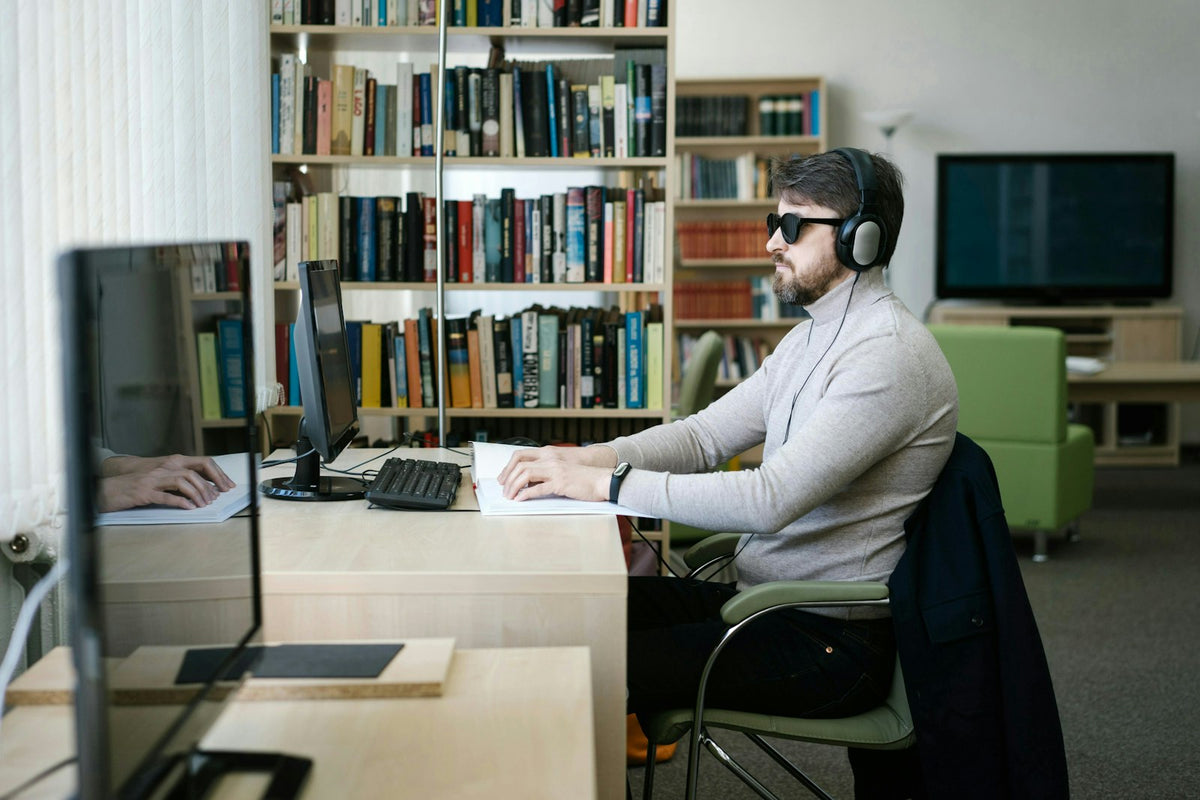 Homme malvoyant travaillant sur ordinateur avec un casque audio et des technologies d'assistance